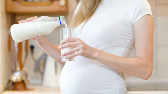 Беременная женщина наливает молоко в стакан